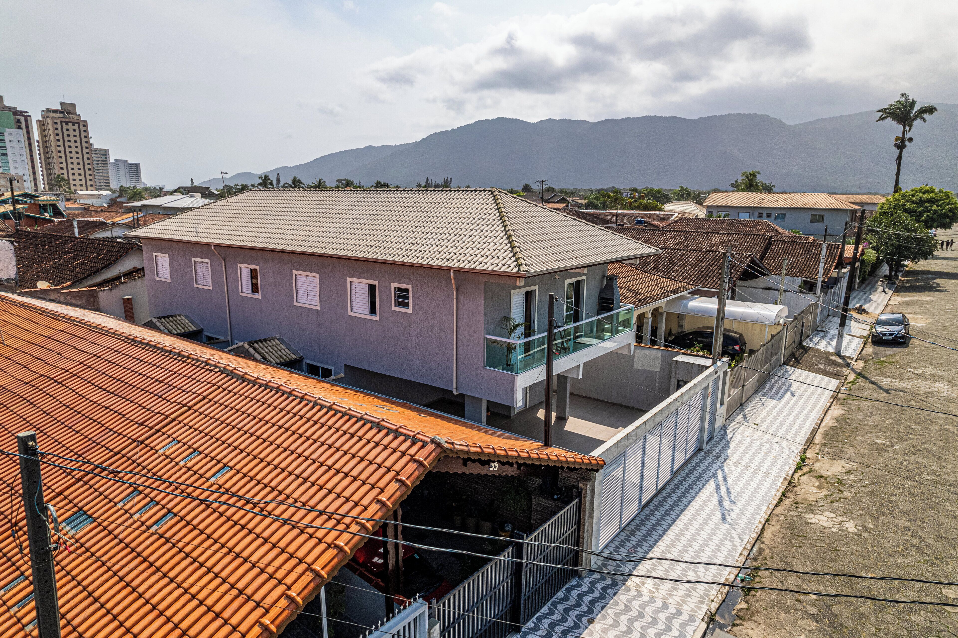 A residential building with a tiled roof, a balcony, and a paved ground.