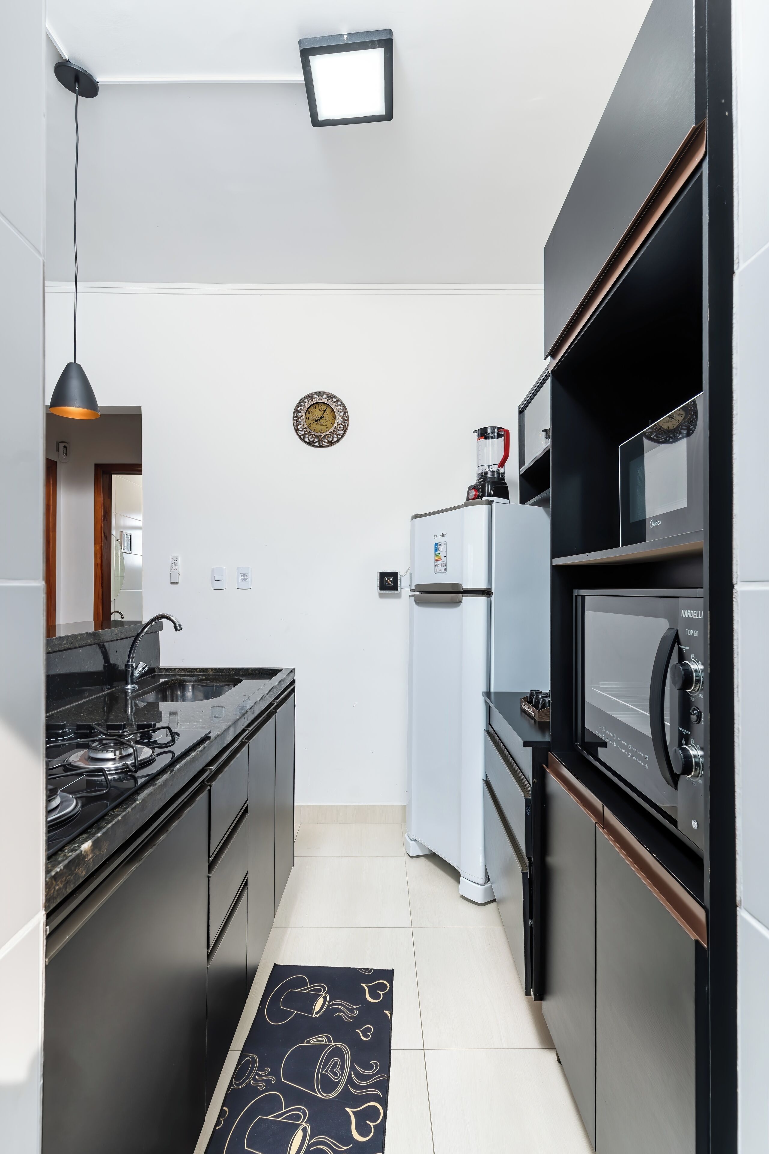 Une cuisine moderne avec un plan de travail noir, des appareils en acier inoxydable et un tapis à motifs noir et blanc.