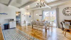 Une salle à manger spacieuse, agrémentée d’un lustre, d’un parquet en bois et d’un tapis à motifs.