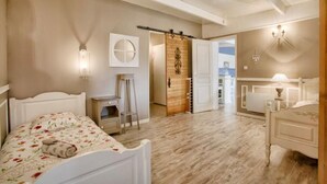 Une chambre à coucher comprenant un lit, une commode, une table de chevet, une porte en bois et un couloir menant à la cuisine.
