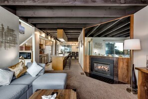 Ein modernes Wohnzimmer mit Kamin, im Hintergrund eine Küche und eine Treppe, die zu einer oberen Ebene führt.