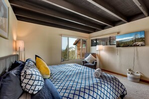 Une chambre avec un grand lit, une chaise, un téléviseur et une fenêtre donnant sur un beau paysage.