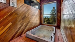 A wooden cabin with a hot tub, wooden walls, and a window with a view of trees. - Entire Townhouse in Lake Village with Stunning Lake View! (Glenbrook)