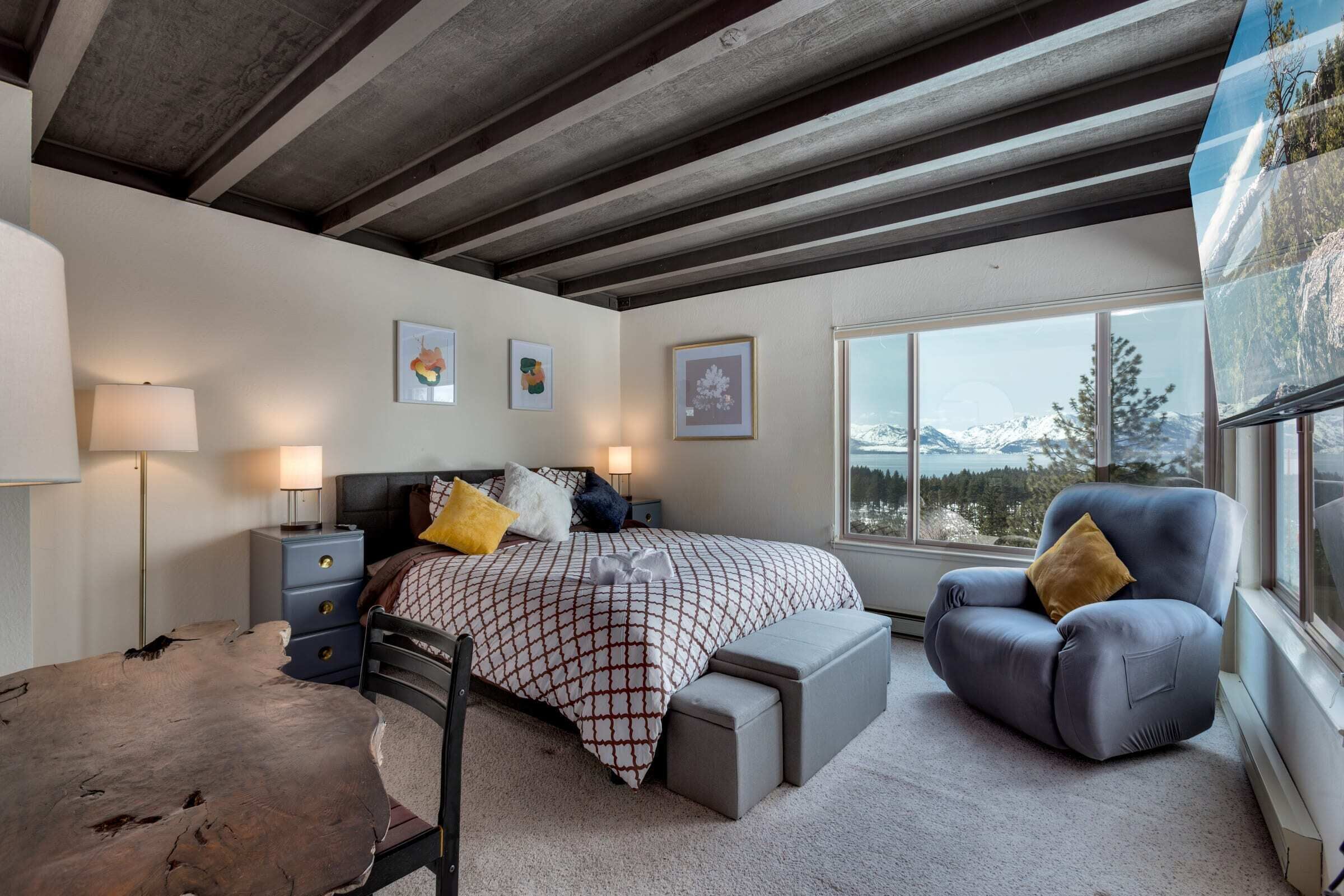 Una camera da letto con un letto, comodini, una sedia, una scrivania e un'ampia finestra con vista sulle montagne.