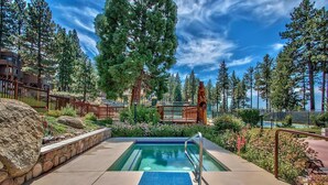 A pool area with a clear blue pool, surrounded by a wooden fence, large rocks, and lush greenery. - Entire Townhouse in Lake Village with Stunning Lake View! (Glenbrook)