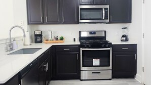 A modern kitchen with dark cabinets, a stainless steel microwave, a gas stove, and a dishwasher. - Experience Austin from this impressive 2,000 sq. ft. Two-Story Home. Designed for groups and professionals, this property offers a versatile layout with a charming backyard and functional dining area. (Austin)