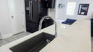 A modern kitchen with a stainless steel sink, black appliances, and a white speckled countertop. - Experience Austin from this impressive 2,000 sq. ft. Two-Story Home. Designed for groups and professionals, this property offers a versatile layout with a charming backyard and functional dining area. (Austin)