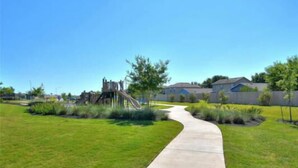 A concrete pathway leading to a playground with a slide and climbing structures, surrounded by well-maintained grass and residential houses. - Experience Austin from this impressive 2,000 sq. ft. Two-Story Home. Designed for groups and professionals, this property offers a versatile layout with a charming backyard and functional dining area. (Austin)