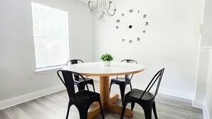 A dining area with a round table, four black chairs, a potted plant, and a wall clock. - Experience Austin from this impressive 2,000 sq. ft. Two-Story Home. Designed for groups and professionals, this property offers a versatile layout with a charming backyard and functional dining area. (Austin)