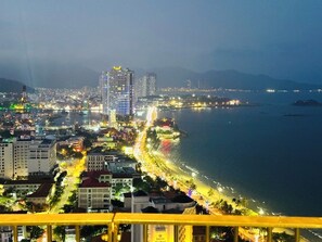 A coastal cityscape at night with illuminated buildings, a beach, and a bridge.