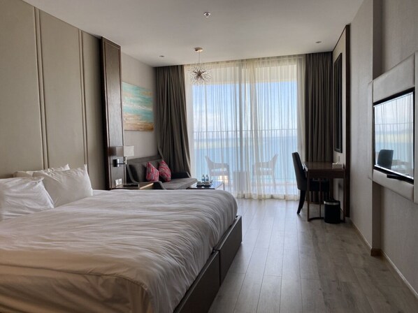 Quarto de hotel moderno com uma cama grande, uma escrivaninha e vista para o mar.