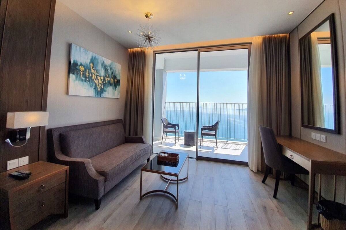 Habitación de hotel moderna con sofá, escritorio, silla y balcón con vista al mar.