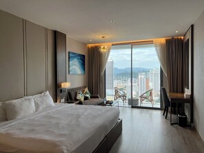 A modern hotel room with a large bed, a desk, and a balcony with a city view. - Nha Trang Monaco Apartment Panorama (Nha Trang)