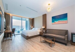 A modern hotel room with a large bed, a sofa, a desk, and a balcony with a view. - Nha Trang Monaco Apartment Panorama (Nha Trang)