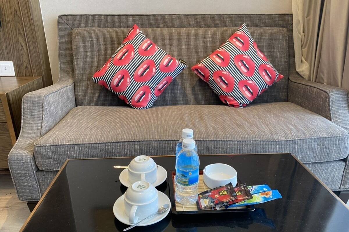 Una sala de estar moderna con un sofá gris, dos almohadas estampadas, una mesa de centro negra con juego de té, una botella de agua y una bandeja con aperitivos.