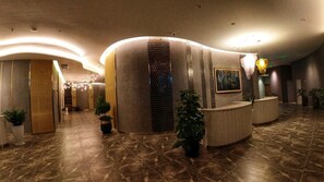 A hotel lobby with a curved reception desk, potted plants, and a tiled floor. - Nha Trang Monaco Apartment Panorama (Nha Trang)
