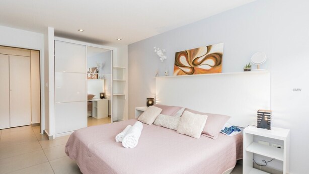 Une chambre à coucher moderne avec un grand lit, une armoire et une table de chevet avec une lampe.