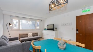 Un salon moderne avec un canapé, une table à manger et des chaises, un téléviseur et un panneau indiquant la sortie de secours, marqué « SALIDA ».
