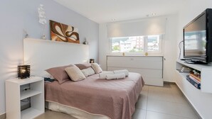 Une chambre moderne avec un lit, des tables de chevet, un téléviseur et une fenêtre donnant sur la ville.