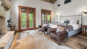 Une chambre à coucher rustique avec un grand lit, des fauteuils en cuir, un plancher en bois et un mur en pierre.