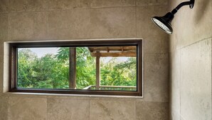 Une salle de bain avec une fenêtre, une pomme de douche et une vue sur les arbres.