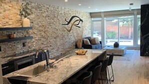 A modern kitchen with a stone backsplash, a central island with bar stools, and a large window providing natural light. - Fully Remodeled Luxury 1BR | Gondola • A/C • Steam Shower (Telluride)