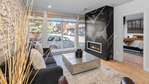 A modern living room with a fireplace, a large window, and a view of the street. - Fully Remodeled Luxury 1BR | Gondola • A/C • Steam Shower (Telluride)