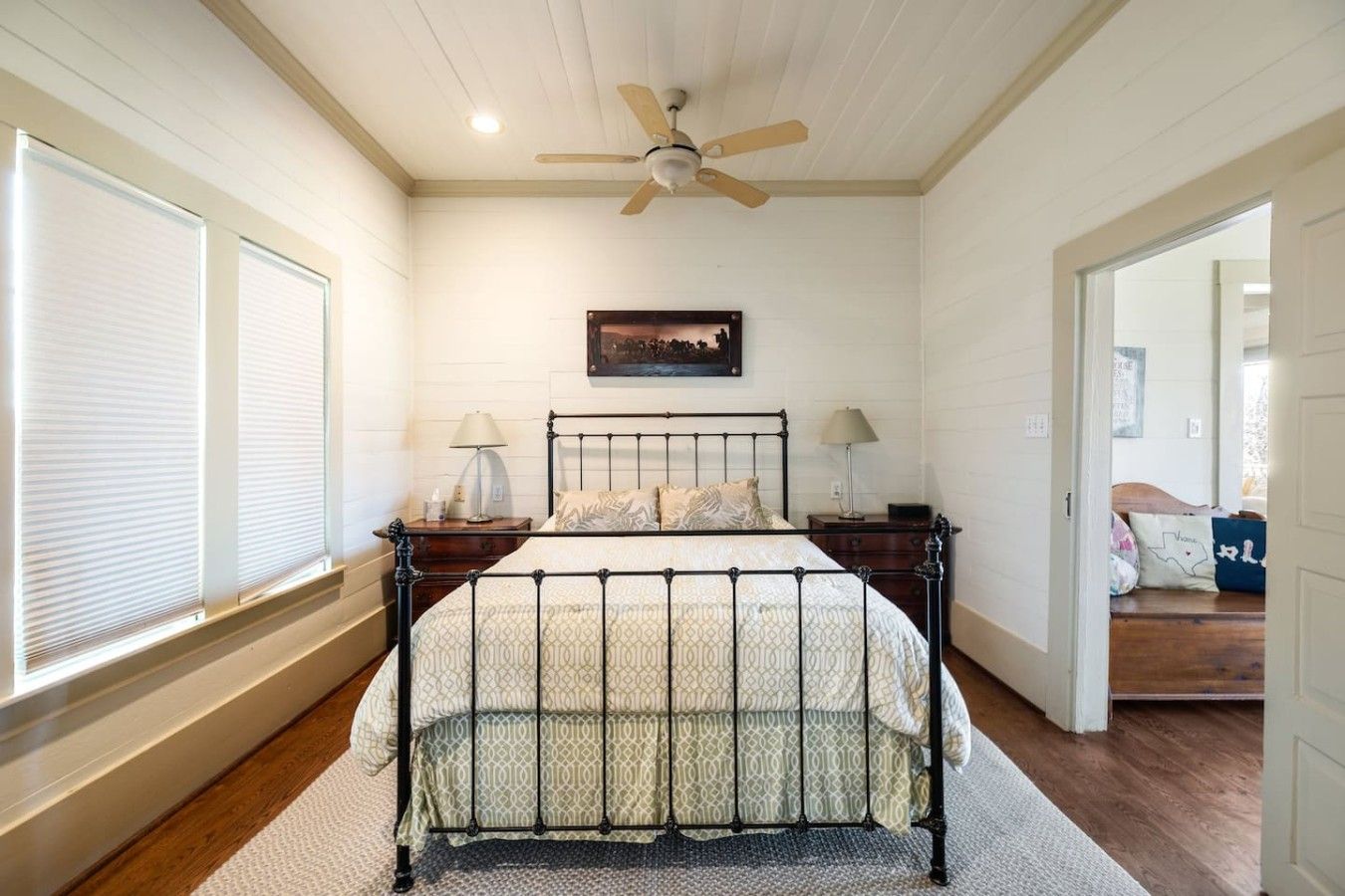 A bedroom with a bed, two bedside tables, a ceiling fan, and a window with blinds.