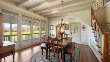 A spacious dining area with a wooden table and chairs, a chandelier, and a view of a green landscape through large sliding glass doors.
