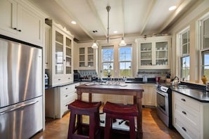 A spacious kitchen with white cabinetry, a stainless steel refrigerator, a wooden island with stools, and a large window providing natural light. - Cozy Ranch Home minutes from Brenham, Bellville, Round Top! (Brenham)
