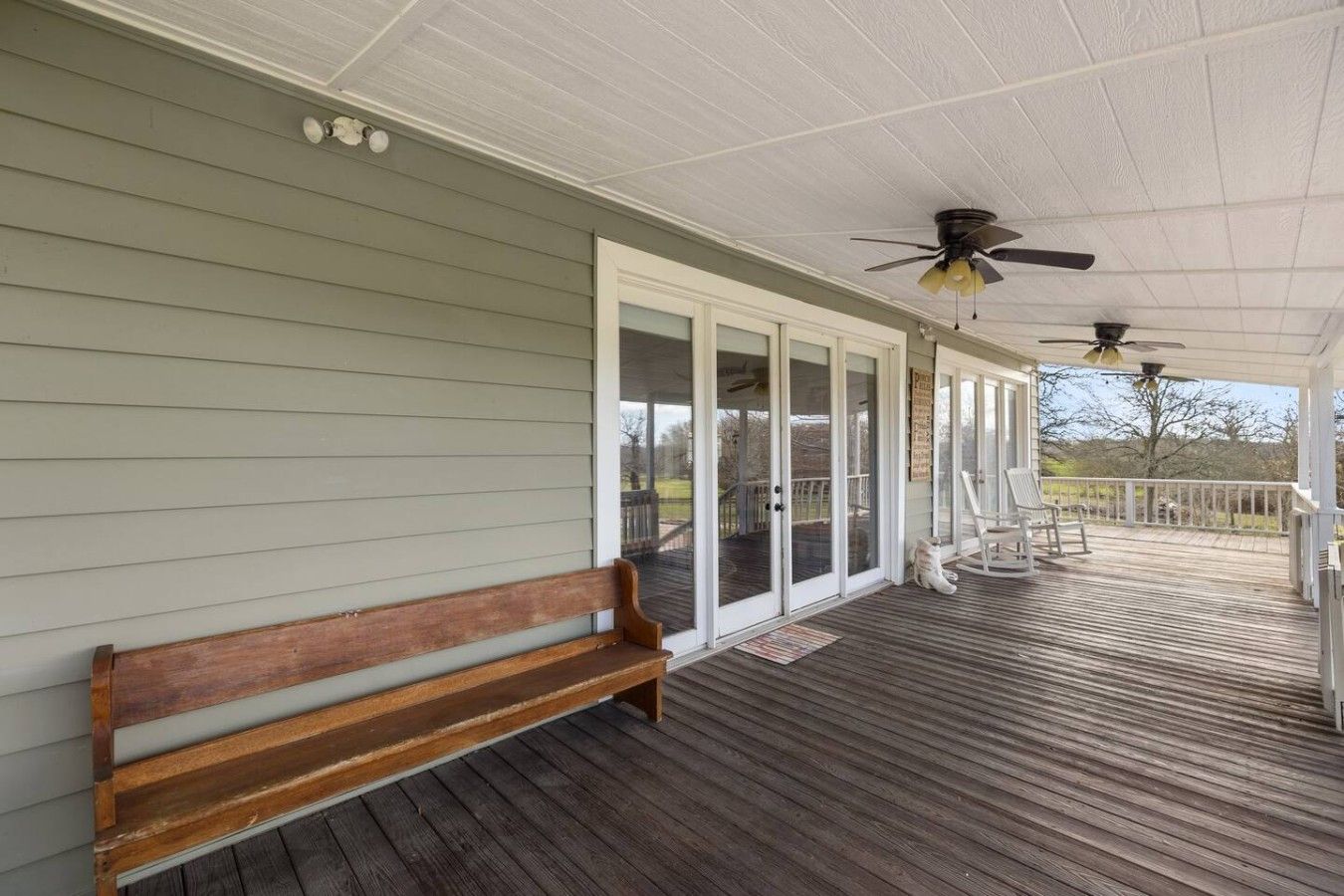A covered porch with a wooden bench, a ceiling fan, and a view of the outdoors.