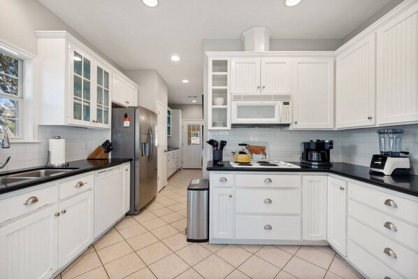 A modern kitchen with white cabinetry, a stainless steel refrigerator, a microwave, and a coffee maker.