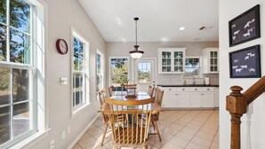 Una cocina amplia con armarios blancos, un comedor con sillas de madera y grandes ventanas que ofrecen vistas al exterior.