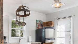 A rustic kitchen with a wooden table, two chairs, a hanging light fixture, and a window with a view of greenery. - Rustic Charm in our Quaint Round Top Farmhouse! (Round Top)