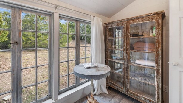 A room with large windows, a rustic wooden cabinet, and a round table with a book. - Rustic Charm in our Quaint Round Top Farmhouse! (Round Top)