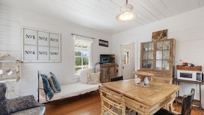 A cozy room with a wooden dining table, a sofa with cushions, a birdcage, and a sign labeled "WINE". - Rustic Charm in our Quaint Round Top Farmhouse! (Round Top)