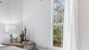 A bedroom with a large bed, a vintage clawfoot bathtub, a dresser, and a window with a view of trees. - Rustic Charm in our Quaint Round Top Farmhouse! (Round Top)