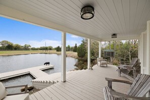 A covered outdoor deck with a pond, chairs, and a pig. - Lakefront Charm: Your Perfect Getaway in Round Top (Fayette County)