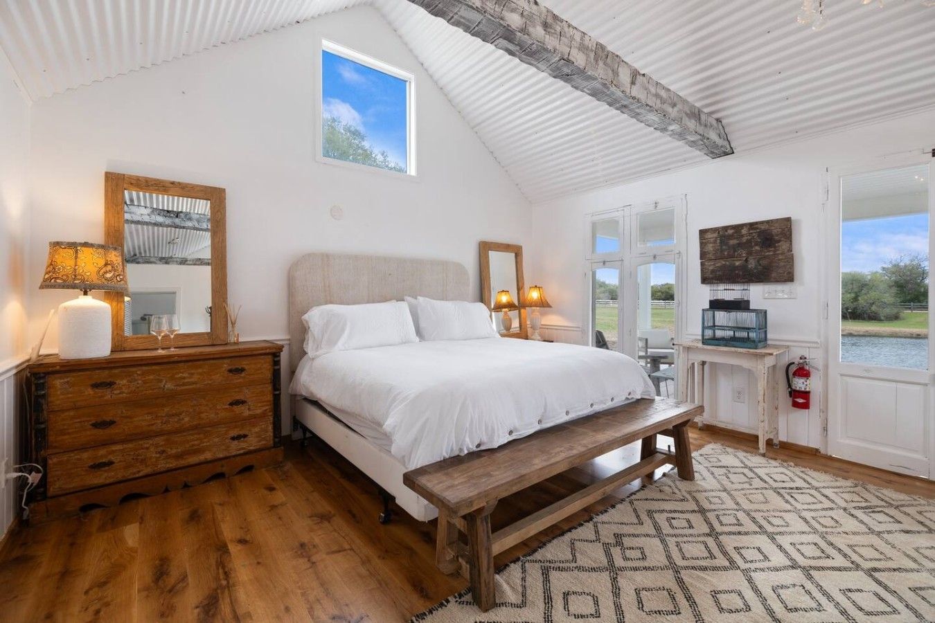 Een slaapkamer met een bed, een houten dressoir, nachtlampen, een bankje en uitzicht op het omliggende landschap.