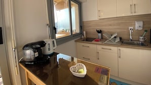 Una cucina compatta con una finestra, un bollitore, una macchina per il caffè, un lavandino e un piccolo piano di lavoro con un cesto.