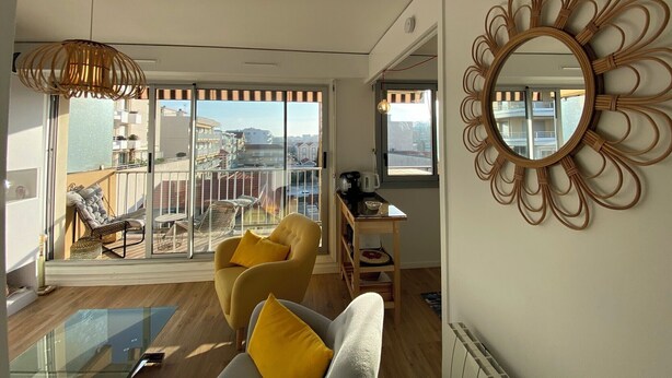 Un soggiorno moderno con una porta scorrevole in vetro che dà su un balcone, uno specchio rotondo e una poltrona gialla.