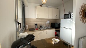 Una cucina compatta con mobili bianchi, un forno a microonde nero, un frigorifero bianco e una macchina per il caffè.