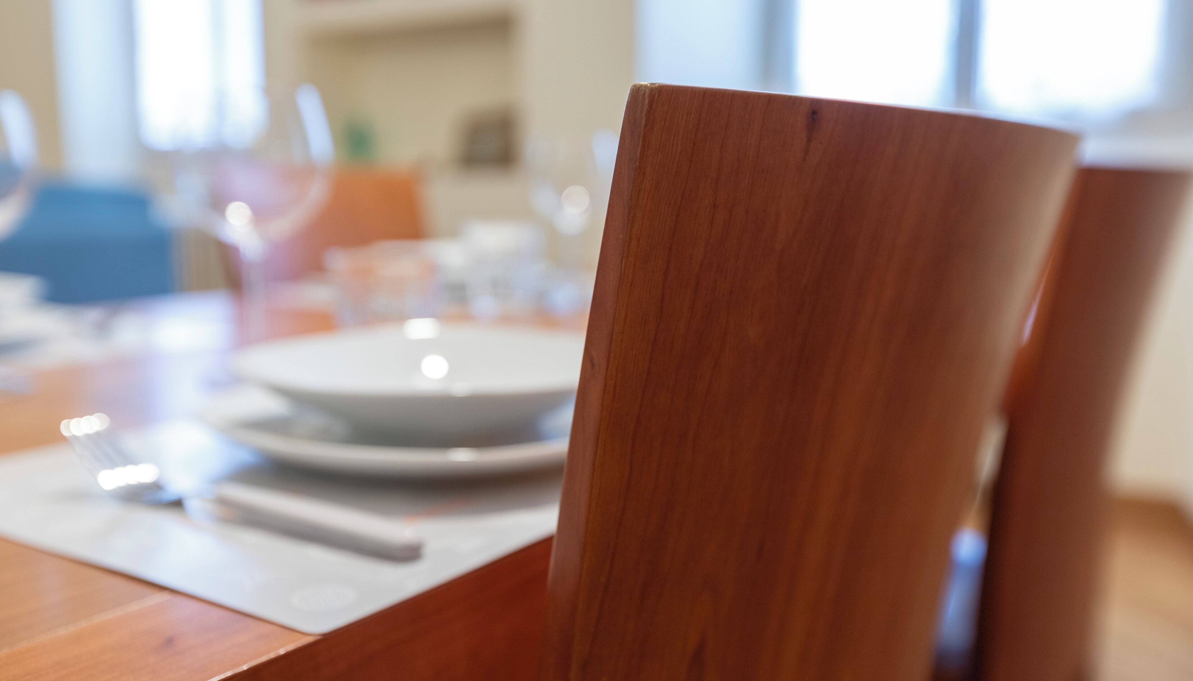 A wooden dining table with a white placemat and a white plate.