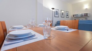A dining table set with plates, glasses, and cutlery, with a blue couch and a bookshelf in the background.