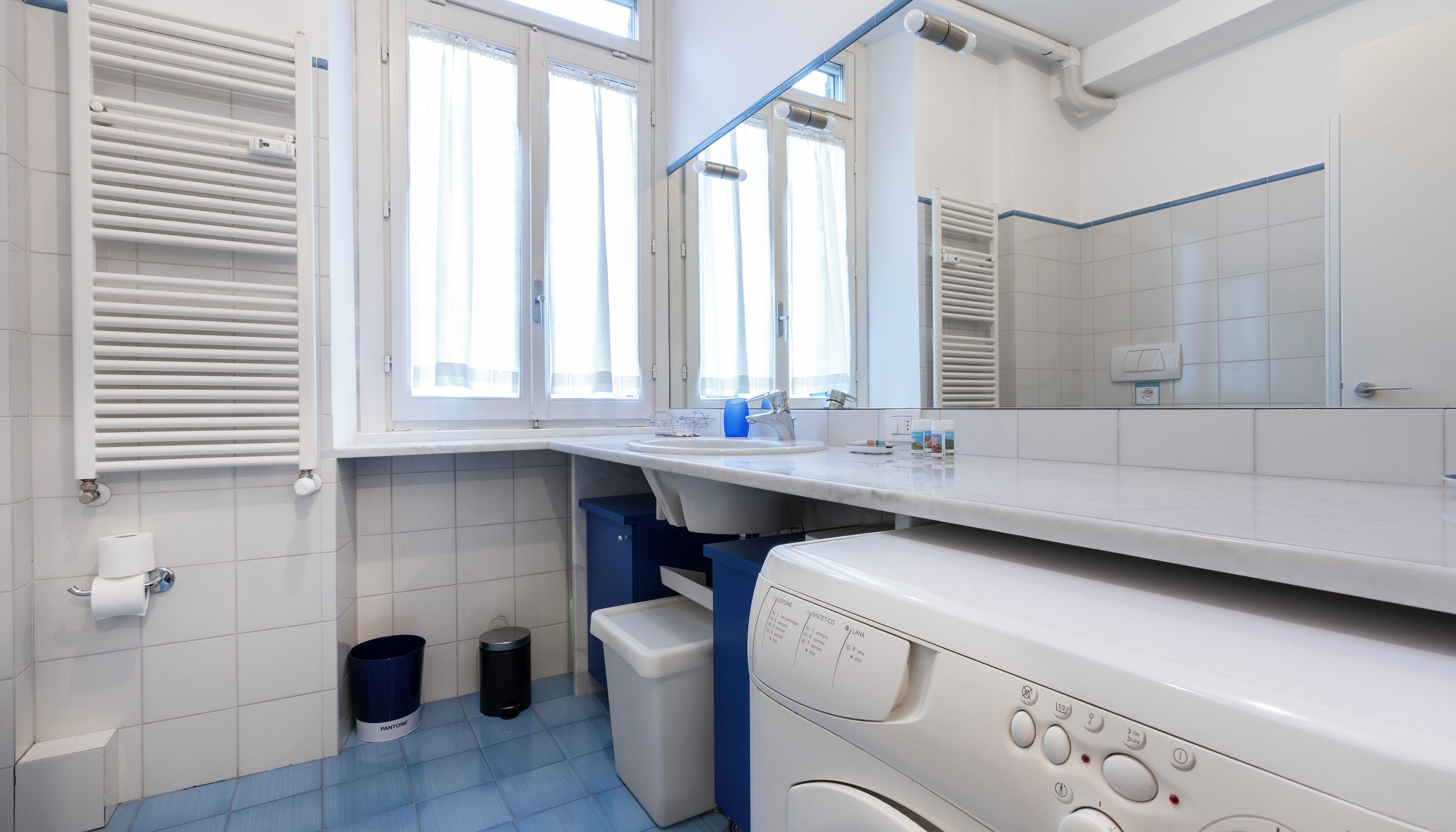 Un bany modern amb un lavabo blanc, un mirall i una rentadora integrada.