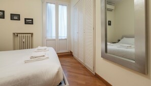 A hotel room with a bed, a large mirror, a radiator, and a window with curtains.