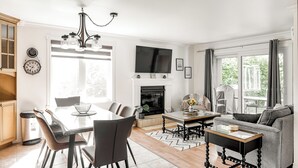 A modern living room with a fireplace, a dining area with a table and chairs, and a sofa. - Cozy 3 bedroom  condo in Magog with a semi private loft.Great location. (Magog)