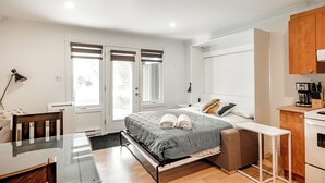 A modern bedroom with a bed, bedside table, and a small kitchenette. - Cozy 3 bedroom  condo in Magog with a semi private loft.Great location. (Magog)