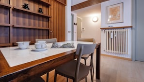 A dining area with a wooden table, chairs, and a white tiled floor. There are shelves with decorative items and a framed picture on the wall. - Italianway - Eschilo 5 (Milan)