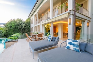 Una casa a due piani con un balcone, area salotto esterna e piscina.